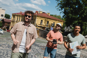Wall Mural - positive multiethnic tourists with vintage camera and map smiling during excursion with tour guide o