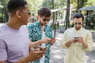 Wall Mural - african american man looking at trendy friends chatting on mobile phones in summer park.