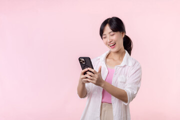 Pretty young asian woman showing success, victory hand gesture while receiving great news from smartphone on pink background. Happy technology, mobile phone advertisement, online application concept