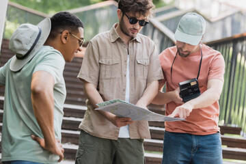 Wall Mural - man with vintage camera pointing at city map in hands of friend on stairs in city.