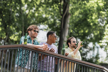 Wall Mural - african american man in sunglasses talking to friends near beer on railing in summer park.