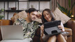 © saksit - Young couple using tablet and laptop together on sofa in living room at home