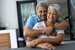© Wavebreak Media - Portrait of smiling romantic biracial senior man embracing wife from behind sitting at table at home