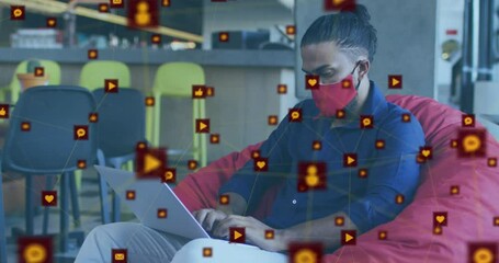 Poster - Animation of network of digital icons over biracial man wearing face mask using laptop at office
