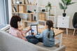 © Sofiia Shunkina - Brunette caucasian woman talking on phone and holding modern gadget in hand while little girl sitting next to her. Young ladies ordering new casual outfit at sales on virtual clothes store website.