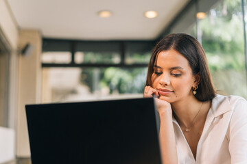 Thoughtful woman in an office. Attractive woman reminiscing while watching a video on her laptop at home