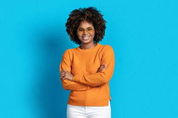 Wall Mural - Positive black woman posing with arms crossed over blue background