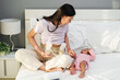 happy mother using breast pump machine to pumping milk while talking with her newborn baby on bed
