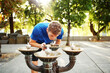 © Cavan Images - Sporty man bending over drinking fountain on footpath