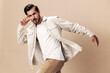 Stylish man smile runs and jumps on a beige background in a white t-shirt and business jacket, flying clothes hero, fashionable clothing style, copy space, space for text
