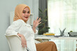 © Prathankarnpap - Friendly asian Muslim woman in in hijab waving hand at camera, greeting someone while sitting in modern office