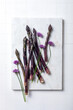 Bunch of fresh purple asparagus with chive flowers on white marble board. Top view, copy space