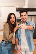 © Jose Calsina - Vertical Young caucasian couple happy to show the keys of their new home looking at camera together, Smiling husband and wife opening their new apartment paid for with a mortgage. Relationship concept