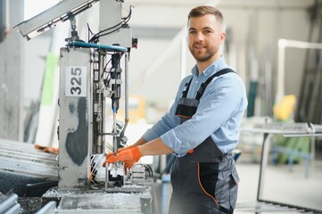 Wall Mural - Portrait of factory worker in protective uniform and hardhat standing by industrial machine at production line. People working in industry