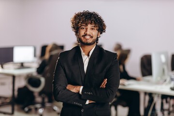 Wall Mural - Excited entrepreneur standing in confident pose in office. Happy businessman posing with crossed arms and looking at camera