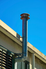 Metal rooftop chimney vent for fireplace or industrial purposes on side of building with blue copy space sky background