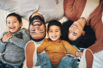 Wall Mural - Happy, above and portrait of a family on a bed for relaxation, bonding and quality time. Laughing, smile and carefree parents with children in the bedroom to relax and play in the morning together