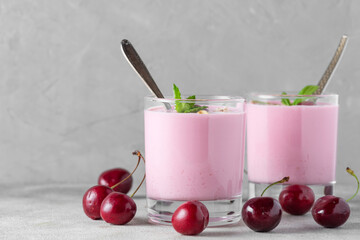 Wall Mural - Two glasses of healthy cherry yogurt with fresh berries, oats, spoon and mint on gray background. Healthy breakfast