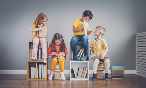 Fototapete - Group of children sitting on the book's stacks and on the bookshelves in the room and reading periodical.