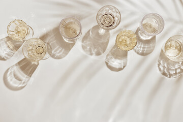 Flat lay with white sparkling wine bottle, set glasses wine with sunshine shadow and flare on light beige background. White wine aesthetic photo, copyspace. Summer holiday monochrome still life