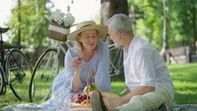 Happy Mature Woman Feeding Husband Grape During Picnic In Summer Park, Date