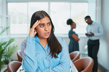 Young woman looks upset while colleagues talk behind her back, office drama