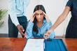 © Meeko Media - Young business woman rubs temples stressed while other colleagues want her input