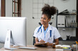 © Parichat - Portrait of female African American doctor sitting in her office at clinic. working with dewsktop computer.