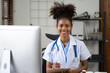 © Parichat - Portrait of female African American doctor sitting in her office at clinic. working with dewsktop computer.