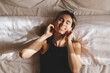 © zvkate - Beautiful young woman listening music in wireless headphones at home lying on bed. Young pretty woman person are happy and enjoy with music by using earphone for listen a sound audio in bedroom.