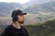 © Chepko Danil - Young man preforms yoga in mountains, Explorer look in summer mountain breathing fresh air, teenager in headphones listening music in nature