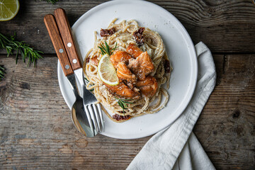 Homemade pasta with baked salmon bites, sun dried tomatoes and creamy lemon sauce on white plate on rustic wooden table.