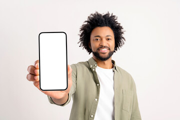 Excited hilarious African American curly young man showing smartphone with empty screen and screaming yes on white background, overjoyed guy won online, celebrating victory