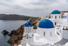 White Churches With Blue Domes In Oia Overlooking The Sea