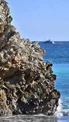 Sticker - View of Praia da Mijona Beach and blue sea surrounded by rocky hills under clear sky in Portugal