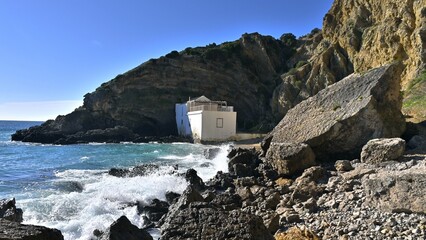 Wall Mural - View of Praia da Mijona Beach and blue sea surrounded by rocky hills under clear sky in Portugal