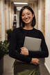 © Drobot Dean - Smiling business woman holding laptop while standing in coworking lobby