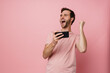 © Drobot Dean - Man making winner gesture while playing online game on mobile phone isolated over pink wall