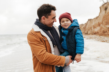 Wall Mural - Joyful father holding his son in his arms during walk on beach