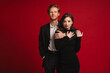 © Drobot Dean - Beautiful couple hugging and looking at camera while standing isolated over red wall