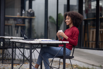 Sticker - Young African American businesswoman with laptop sitting at table outdoor.