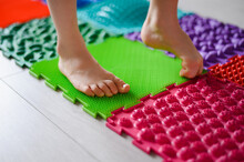 The Child Is Engaged In Orthopedic Massage Mats For Legs Of Different Hardness And Texture. Massage Of The Nerve Endings Of The Legs, Prevention Of Flat Feet In Children. Treatment Of Foot Deformity.
