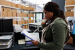 © DC Studio - African american worker talking at landline phone with remote customer discussing order details. Storehouse employee holding clipboard, analyzing goods inventory report in storage room.