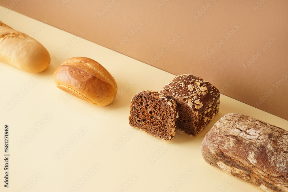 Loaves of different bread on beige table near brown wall
