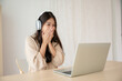 © Monster Ztudio - Young asian woman wearing headset while working on computer laptop at house. Work at home, Video conference, Video call, Student learning online class