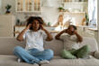 Unhappy irritated African American family mother and son sitting on sofa covering ears annoyed by loud noisy neighbors in poorly insulated apartment, living in house with poor sound insulation