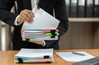 © Phimwilai - Businesswoman in black suit working at desk with documents preparation, searching, sifting through information related to financial, earnings, taxes of company to prepare for meeting in office.