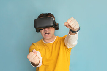 Attractive man with virtual reality glasses paying car simulator on blue background