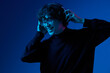 © SHOTPRIME STUDIO - Man teenager wearing headphones listening to music and dancing and singing open mouth smile glasses, hipster lifestyle, portrait blue background, neon light, style trends, mixed light, copying space