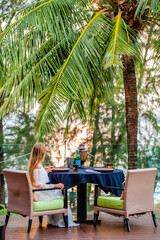 Wall Mural - Unrecognizable woman on dinner in outdoor restaurant with tropical palm trees and sea on background. Travel, exotic vacation concept.